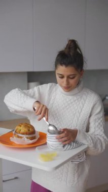 Bir kadın soslu sıcak, lezzetli bir pastanın tadını çıkarır, şık mutfağında sıcak bir kahvaltı anının tadını çıkarır.