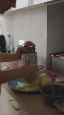 Metal rendeleyici kullanarak güzel tasarlanmış şık bir mutfakta ustalıkla taze patatesleri rendeleyen bir insan.