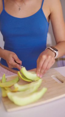 Yetenekli bir kadın, mutfaktaki temiz bir kesim tahtasıyla canlı, taze meyveyi ustalıkla keser ve hazırlar.