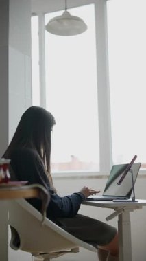 Genç bir kadın, modern üretkenliğin bir örneği olarak, parlak ve iyi aydınlatılmış bir çalışma alanında dizüstü bilgisayarıyla derinden ilgilenir.