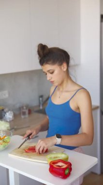 Mükemmel aydınlatılmış bir mutfakta genç bir kadın taze bir salata hazırlamak için canlı kırmızı biberleri ustalıkla dilimliyor.