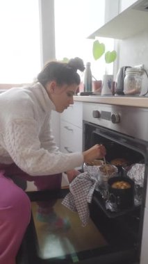 Neşeli bir kadın fırında pişmiş yiyeceklerini kontrol eder, aşçılık becerilerini ve tutkusunu gösterir.