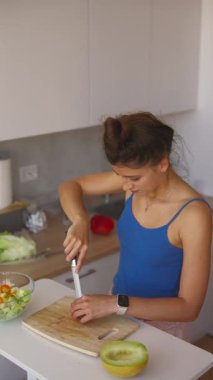 Parlak ve havadar bir modern mutfakta, bir kadın canlı sebzeler kullanarak taze ve renkli bir salata hazırlar.