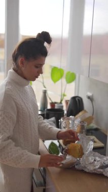 Bir kadın keyifle güzel bir kahvaltı hazırlar. Parlak bir mutfakta, hoş dekorlar ve güzel bitkilerle dolu.