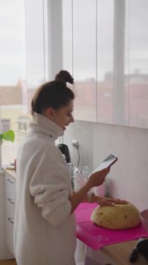 Bir kadın, modern mutfak alanında akıllı telefonunu adım rehberliği için kullanmaktan mutluluk duyar.