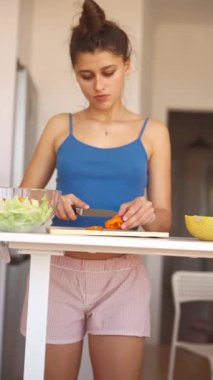 Genç bir kadın şık bir mutfakta lezzetli ve sağlıklı bir yemek için taze sebzeleri dilimlemeye odaklanır.