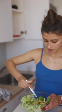 Renkli bir salata hazırlayan bir kadın sağlıklı beslenme ve parlak bir mutfakta pişirme becerilerini ön plana çıkarıyor.