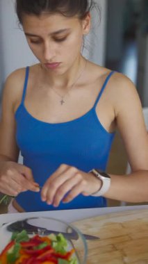 Genç bir kadın, sıcacık mutfağında sağlıklı beslenme alışkanlıklarını kutlamak için canlı ve taze bir salata hazırlıyor.