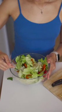 Genç bir kadın kasede taze bir salata hazırlıyor. Modern bir mutfakta sağlıklı yemek hazırlıyor..