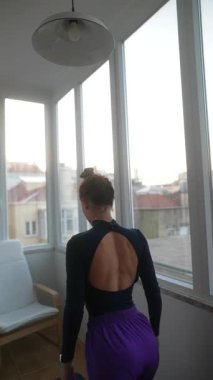 Nefes kesici manzaralı geniş ve aydınlık bir odada, bir kadın zarif bir şekilde çeşitli yoga pozları veriyor.