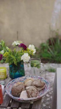 Canlı çiçeklerle dolu güzel bir açık hava sahnesi ve kırsal bir masada taze pişmiş ekmek çeşitleri.