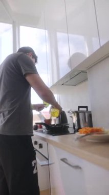 Yetenekli bir aşçı modern bir mutfakta yemek pişiriyor, taze sebzelere yağ ekliyor, lezzetlerini arttırıyor.