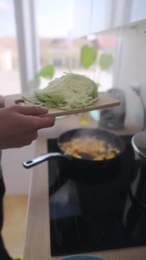 Enerjik ve dinamik bir mutfak sahnesi. Canlı taze lahana ustalıkla lezzetli bir tavaya ekleniyor.