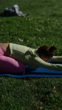 Barışçıl bir açık havada, bir kadın yoga minderinin üzerinde zarifçe uzanır yemyeşil ile çevrili.