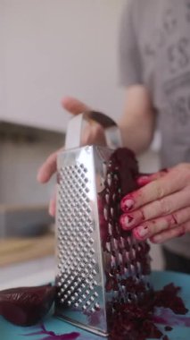 Bir insan taze, renkli pancarları rendeliyor, elleri canlı renklerle lekelenmiş, yemek hazırlama sürecini sergiliyor.