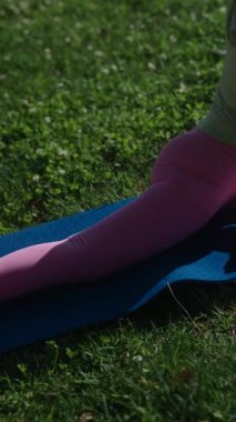 Bir kadın sıcak güneşin altında yemyeşil çimlerle çevrili açık havada zarif bir yoga minderine uzanır.