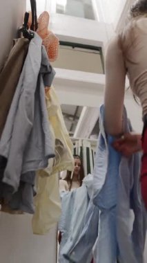 Bir kadın soyunma odasında, askılarda asılı kıyafet koleksiyonundan çeşitli giysiler deniyor.