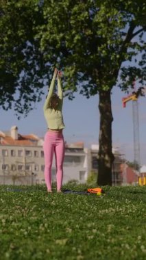 Canlı genç bir kadın güneşli bir parkta zarifçe uzanır. Açık hava sporu ve pozitif enerjiyi kucaklar.