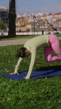 Güzel manzaralı bir parkta, bir kadın yoga yapmaktan son derece zevk alır, inanılmaz gücünü ve esnekliğini gösterir.