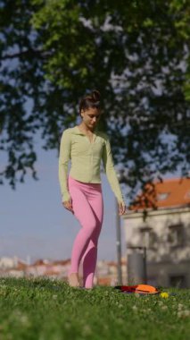 Güzel bir parkta yoga yapan bir kadın esnekliğini ve dengesini sakin bir ortamda sergiliyor.