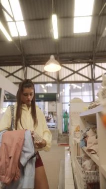 Şık, modaya uygun genç bir kadın şık giysi seçenekleriyle dolu şık bir mağazada geziniyor.