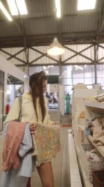 Bir kadın canlı ve canlı bir mağaza ortamında alışveriş yaparken çeşitli şık ürünleri hevesle keşfeder.