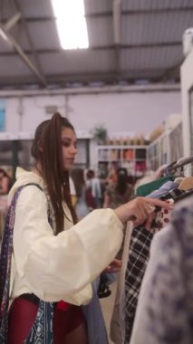 Genç bir kadın, cazibe saçan modaya uygun ve şık bir vintage mağazasında çeşitli elbise raflarını karıştırıyor.