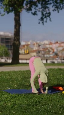 Yeşillik ve şehir siluetiyle dolu canlı bir parkın temiz havasında yoga yapan bir insan.