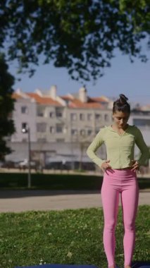 Genç bir kadın yoga çalışmalarını güneşli bir parkta yapıyor. İnanılmaz esnekliğini ve gücünü gösteriyor.