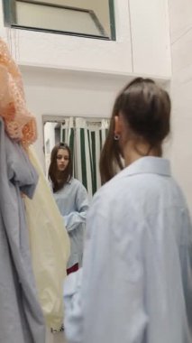 Genç bir kadın, aynadaki yansımasına hayran olduğu için çeşitli büyük beden gömlekler deniyor.