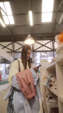 Genç bir kadın, telefonuyla konuşurken bir vintage mağazasında bulunan çeşitli eşsiz eşyalar keşfediyor.