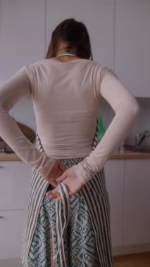 Modern bir mutfakta, bir kadın şık eteğini bağlar, zarif ve rahat elbisesini giyer.