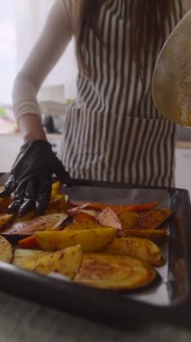 Bir insan sıcak, iyi aydınlatılmış bir mutfakta fırında pişirme tepsisinde canlı sebzeler hazırlıyor.