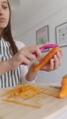 Bir kız parlak, modern bir mutfakta taze havuç soyarken ustaca ev yemeklerini soyardı.