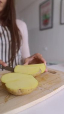 Renkli bir mutfakta, usta bir aşçı titizlikle taze organik patatesleri ahşap bir kesme tahtasıyla dilimler.