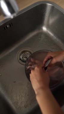 Bir kadın mutfak lavabosundaki çeşitli malzemeleri yıkayarak özenle yemek hazırlıyor.