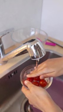 Modern bir mutfak lavabosunda, bir birey titizlikle vişneli domatesleri akarsu akıntısı altında yıkar.