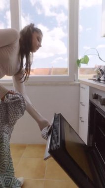 Güneşli bir mutfakta, yetenekli bir kadın fırından lezzetli kızarmış sebzeler çıkarır.