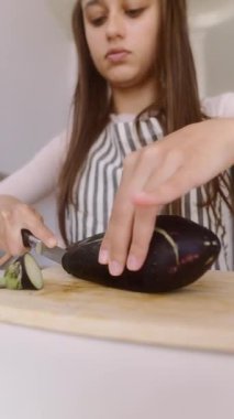 Genç bir kız patlıcanları ustalıkla keserken aynı zamanda şık bir mutfakta yemek yapma becerisini geliştirmeye odaklanıyor.