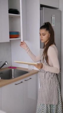 Şık bir önlük giyen bir kadın şık ve modern bir mutfakta taze malzemeler hazırlayıp ev yemeklerini ön plana çıkarıyor.