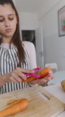 Genç bir kadın şık bir mutfakta taze havuç soyarken etkileyici mutfak becerilerini sergiliyor.