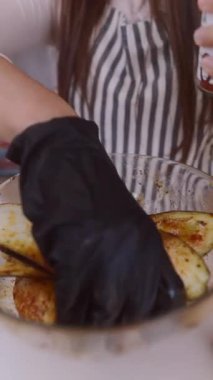 Şef önlüğü giyen biri büyük bir cam kasede çeşitli baharatlarla patates dilimlerini dikkatlice mevsim eder.