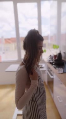 Şık çizgili önlük giyen bir kadın güneşli bir mutfakta çeşitli mutfak işleriyle meşgul.