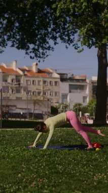 Parkta yoga yapan bir kadın, arkasında bir çocukla güç ve esneklik sergiliyor..