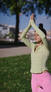 Sakin ve dingin bir genç kadın dışarıda yoga yapıyor. Farkındalık, zindelik ve sağlığına odaklanıyor.