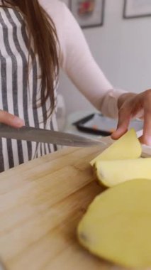 Çağdaş bir mutfak ortamında ahşap bir kesim tahtasıyla patatesleri ustalıkla dilimler..