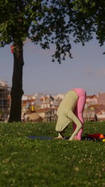 Huzurlu ve pitoresk bir park ortamında, bir kadın zarif bir şekilde vücudunu pembe taytlarla ve yeşil bir bluzla gerer.