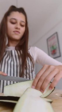 Parlak bir mutfakta, yetenekli bir aşçı ustalıkla taze patlıcanları dilimler, aşçılık uzmanlığını gösterir.