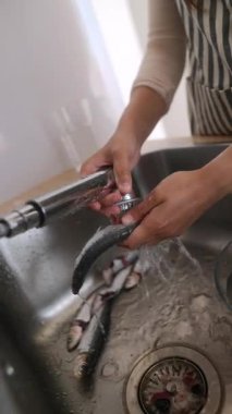 Bir kadın mutfak lavabosundaki taze balıkları özenle temizliyor. Lezzetli ve besleyici bir yemek için özenle hazırlanıyor.