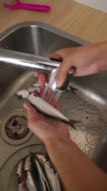 Bir insan mutfak lavabosunda taze balığı iyice yıkıyor ve karmaşık temizlik sürecini canlı canlı gösteriyor.